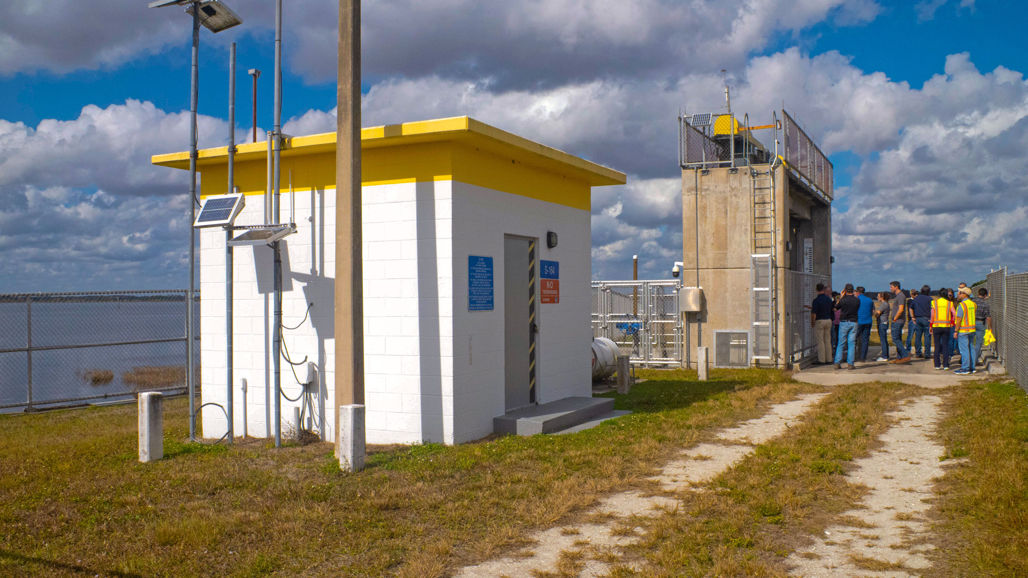 Water flow control station building on Taylor Creek Reservoir with a group of people in the background.